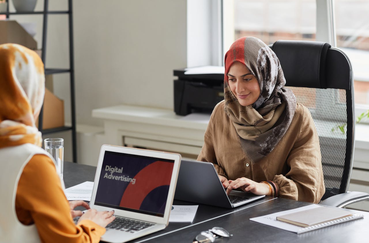 Crafting Captivating Headlines: Your awesome post title goes here Two women in hijabs work on laptops in a bright office. Perfect for business and diversity themes.